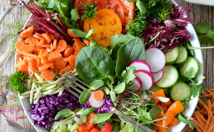 a bowl of vegetables arranged for a salad with a fork resting on top