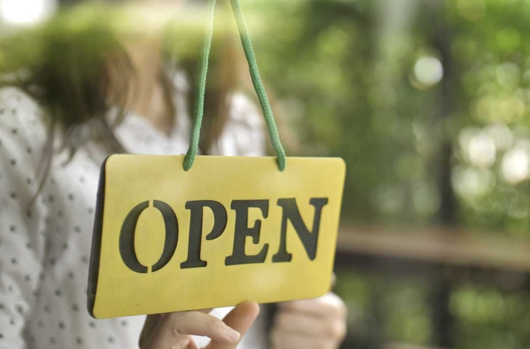 woman blurred in background preparing to flip a focused open sign in the foreground to closed