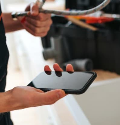 contractor viewing their smartphone in their right hand while holding a hose connector in their left hand