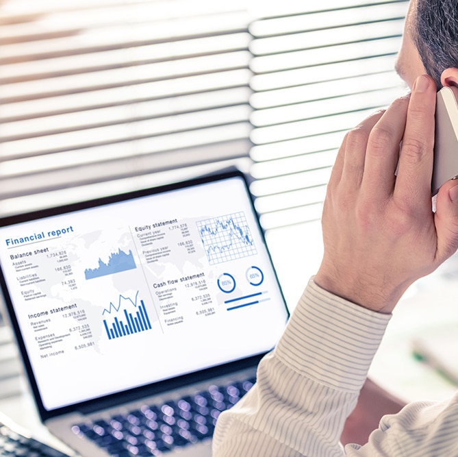 Senior executive manager analyzing a financial report on computer in office and calling on the phone