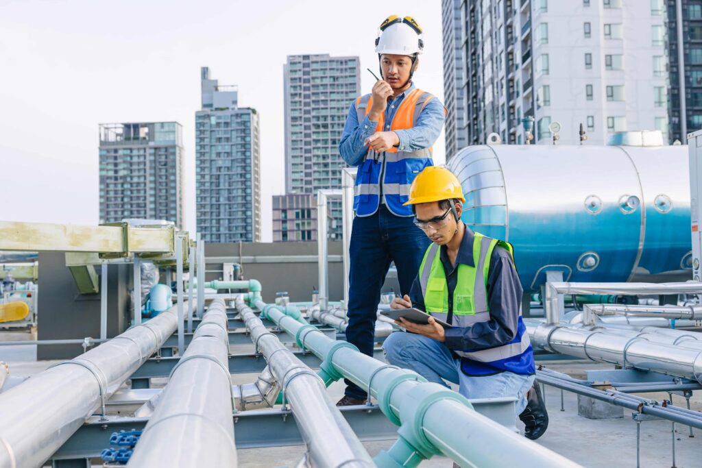 engineer teamwork technician workers service hotel boiler tank hot water supply pipe system. team working safety checking maintenance pipeline heating water delivery line at roof top outdoor.