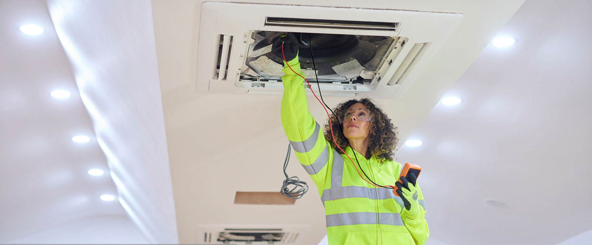 professional female hvac technician on a ladder conducting inspection on ceiling mounted vent