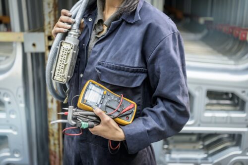 Female apprentice electrician holding equipment in car factory, close up