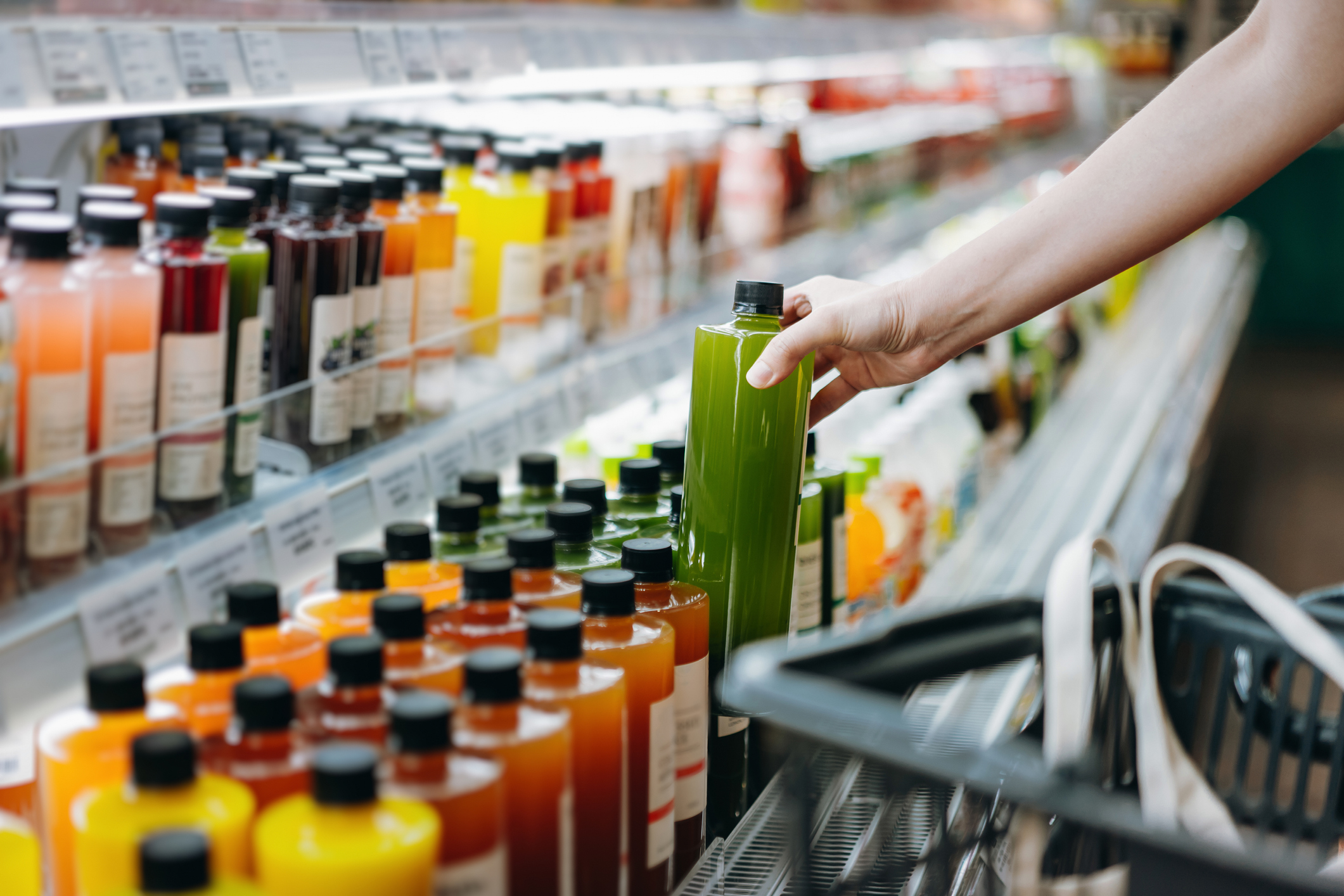 woman shopping for fresh fruit juice from refrigerated shelves in supermarket