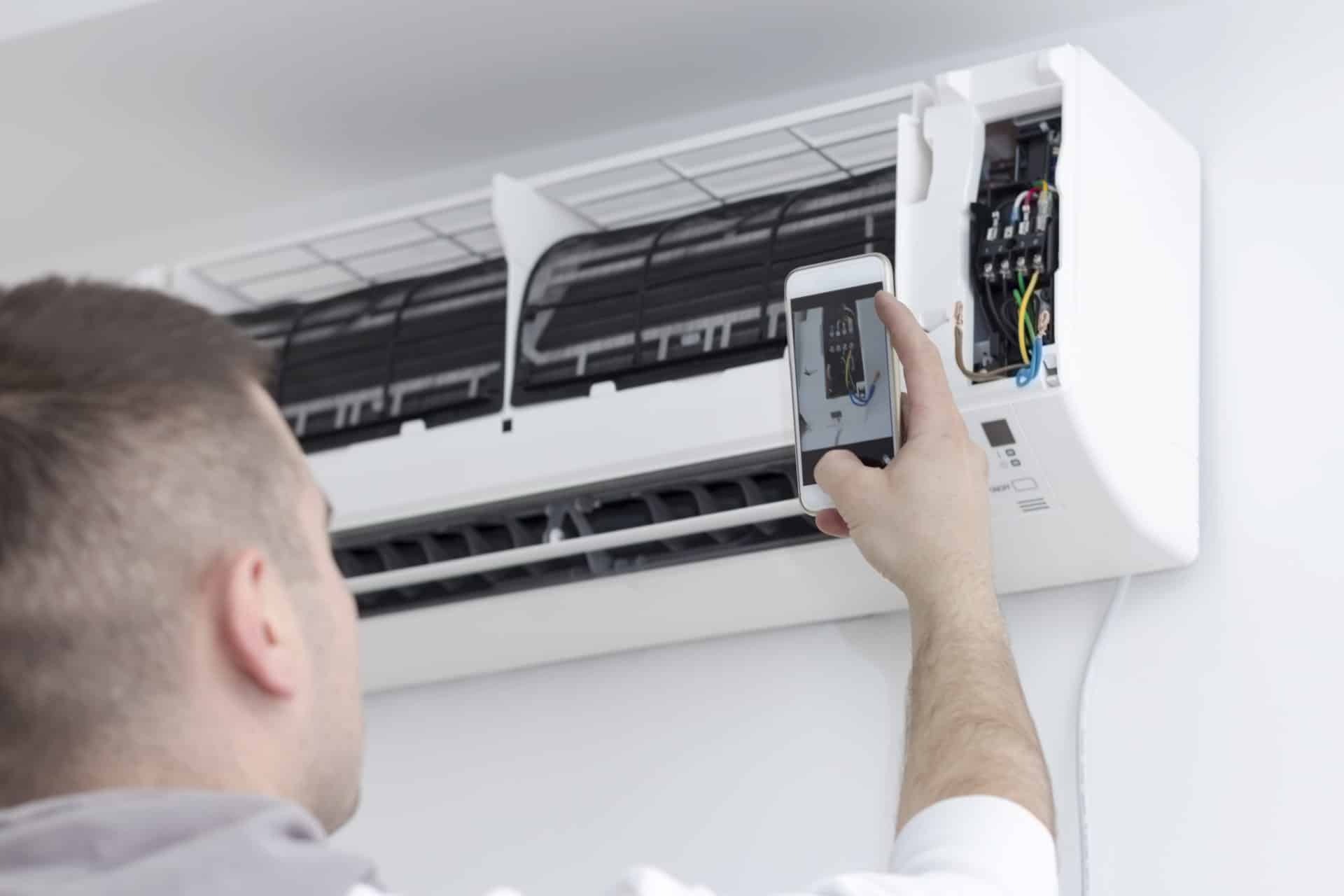 Electrician photographing an installation of air conditioners with smart phone.