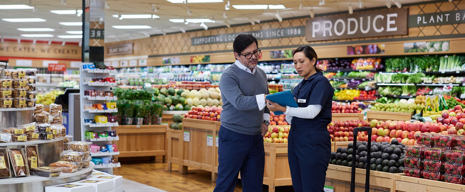 grocery store manager and his employee reviewing produce inventory on a tablet
