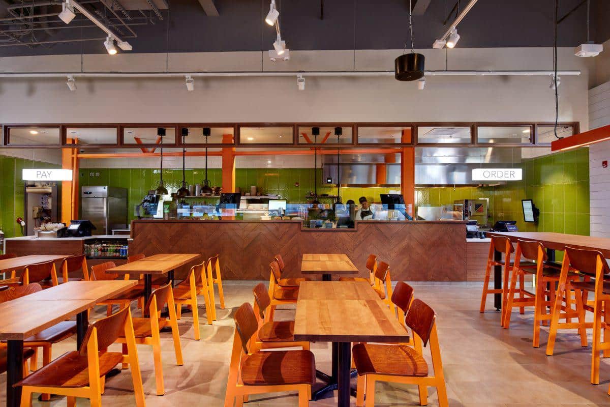 Veggie Grill restaurant interior with an array of wooden tables in front of the grill line