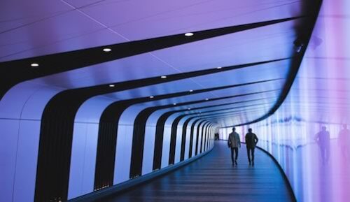 two professionals walking at the end of a winding hallway placed in a futuristic setting