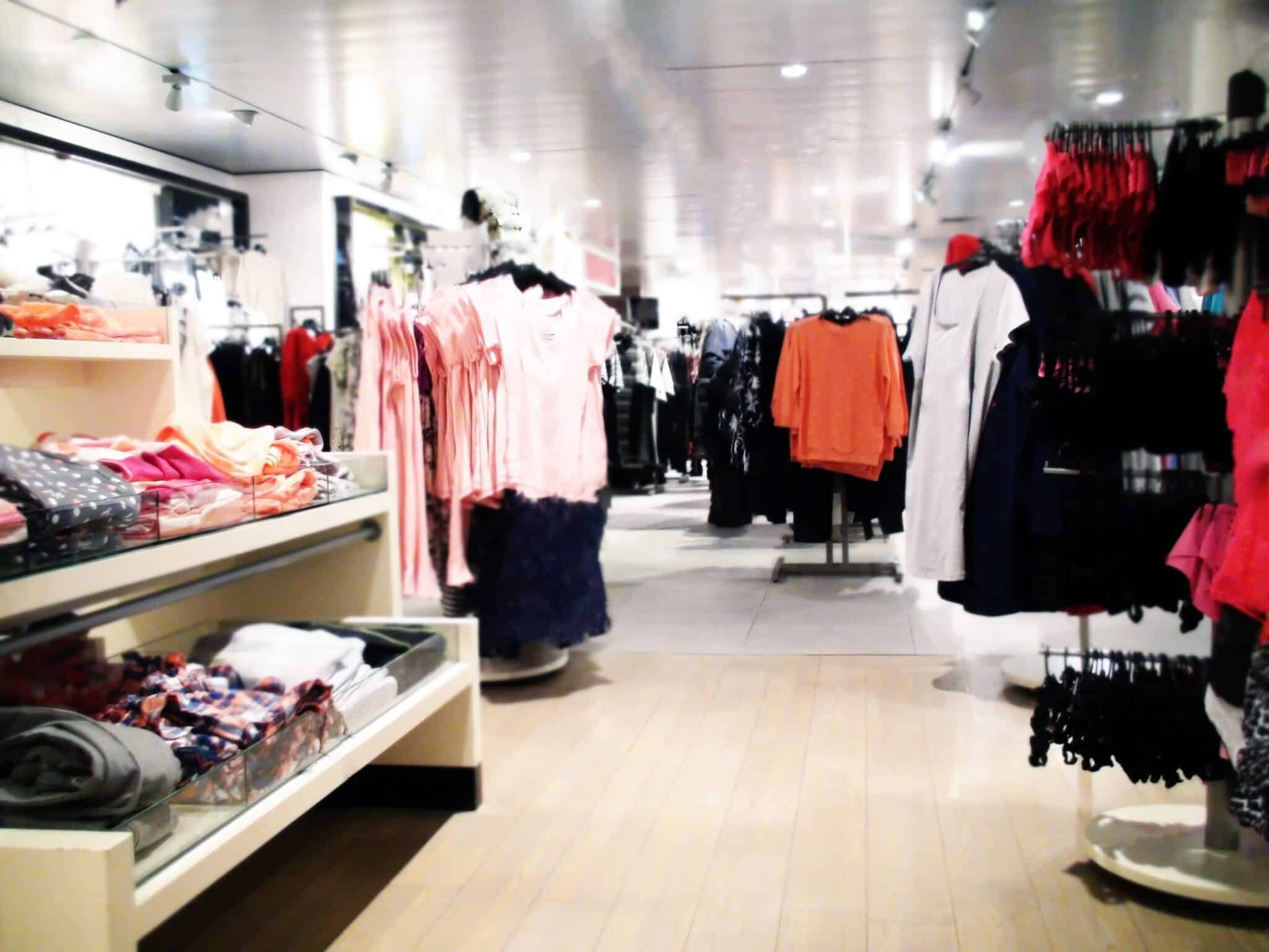 retail clothing store interior with clothes on shelves, tables and racks on display