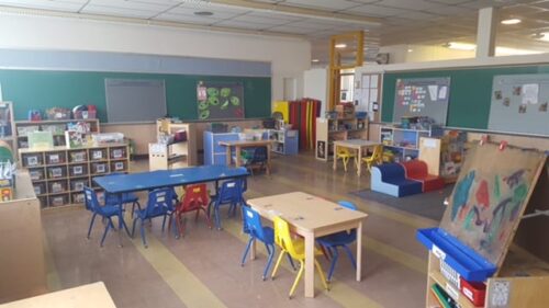 school class room pictured with open floor layout scattered with tables and boards and pictures