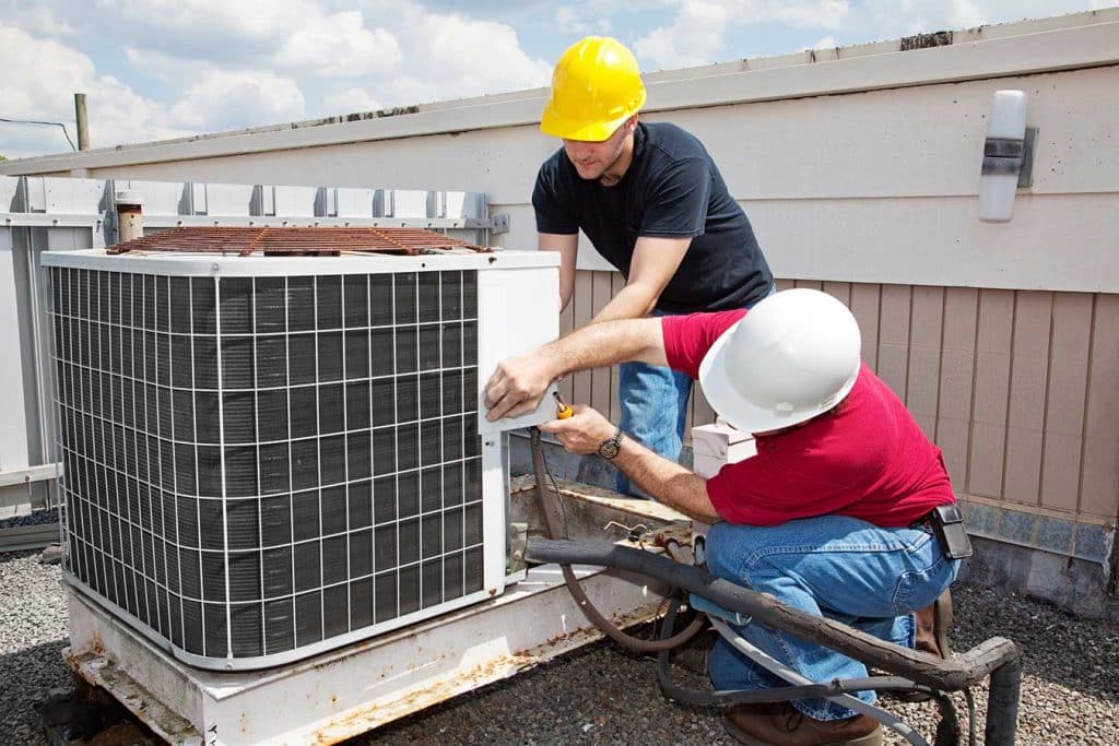 two hvac repair technicians conducting work on a rooftop a/c installation