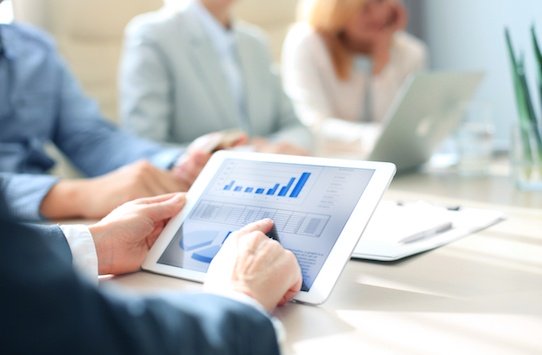 business professional at a board meeting using tablet to view graphs and data