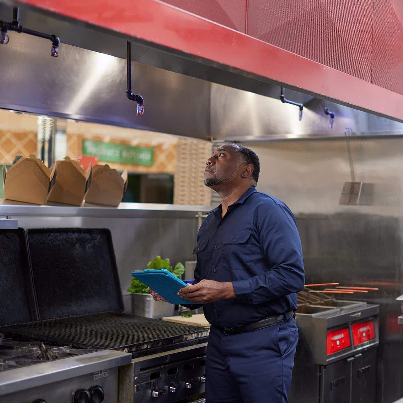 service provider inspecting restaurant hood vent with ipad in hand