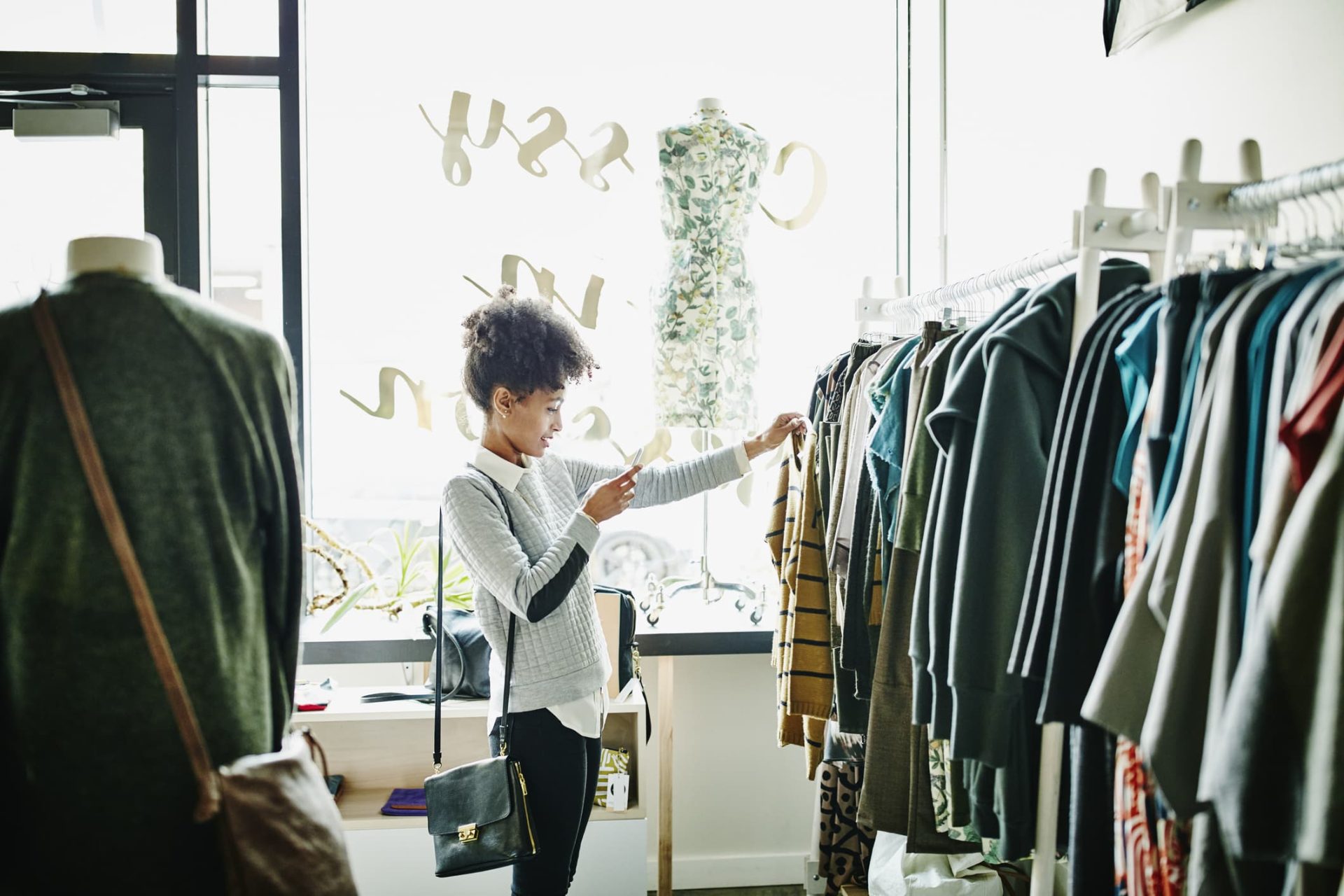 young woman taking pictures of a sweater pulled from a rack on her smartphone within a retail store interior