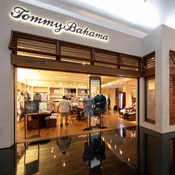 Tommy Bahama storefront with wooden shutters open below a cursive company sign gently backlit