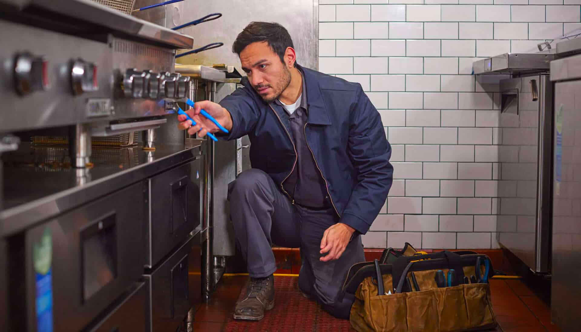 Service provider fixing an oven in a restaurant kitchen.